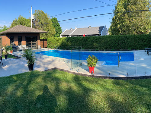Un jardin avec une piscine entourée de rampes en verre.