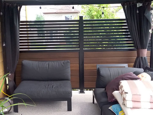 Un patio avec un canapé noir et un rideau noir devant un mur d'intimité, créant une ambiance élégante et moderne.